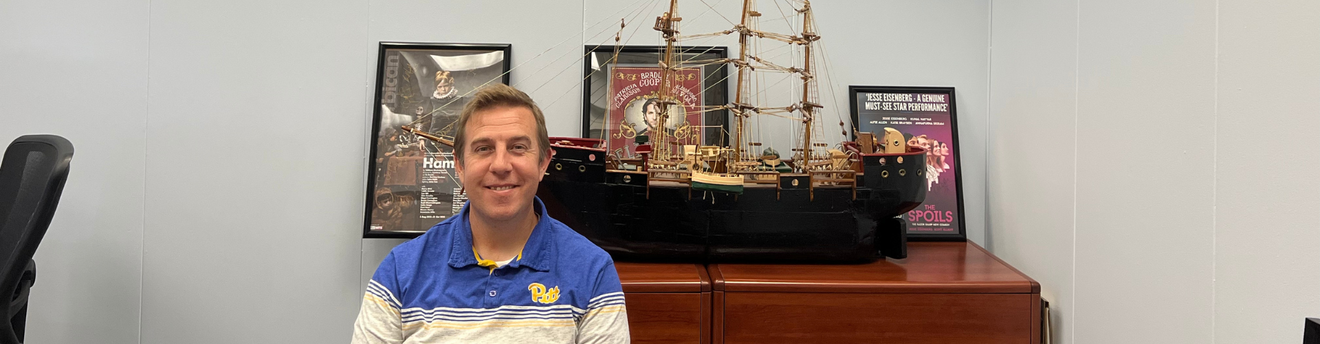 Jeff Whitehead sits in front of large model of ship, with various movie posters on the wall behind him.