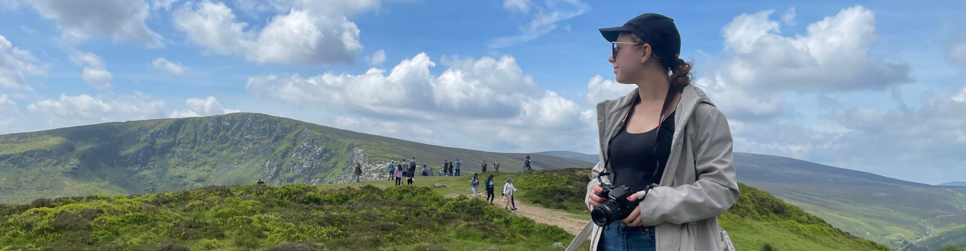 A student with a camera looks over her shoulder across a landscape in Ireland